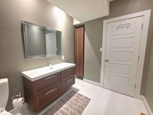 Contemporary bathroom featuring a floating wood-finish vanity with an integrated basin, a rectangular wall-mounted mirror, and white panel doors - 1 Hemlock Close, Fort Saskatchewan, AB 