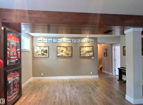 Spacious lower-level room featuring wood-finish flooring, a wood-wrapped beam, recessed lighting, and a white-trimmed window - 1 Hemlock Close, Fort Saskatchewan, AB 