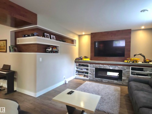 Media console with a stone surround fireplace, built-in shelving, wood-finish flooring, recessed lighting, and an accent wall - 1 Hemlock Close, Fort Saskatchewan, AB 