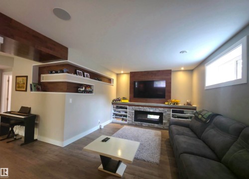 Entertainment space featuring a stone-faced fireplace with an integrated linear electric insert, and wood-finish flooring - 1 Hemlock Close, Fort Saskatchewan, AB 