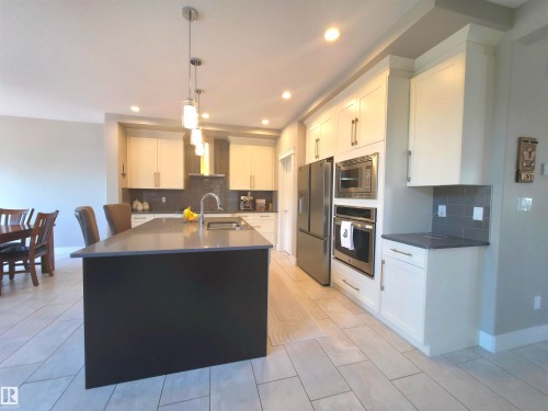Contemporary kitchen featuring a spacious island with a dark base and light countertop, stainless steel appliances, white cabinetry with brushed nickel hardware, gray subway tile backsplash, and light-toned plank tile flooring - 1 Hemlock Close, Fort Saskatchewan, AB 