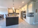 Contemporary kitchen featuring a spacious island with a dark base and light countertop, stainless steel appliances, white cabinetry with brushed nickel hardware, gray subway tile backsplash, and light-toned plank tile flooring - 1 Hemlock Close, Fort Saskatchewan, AB 