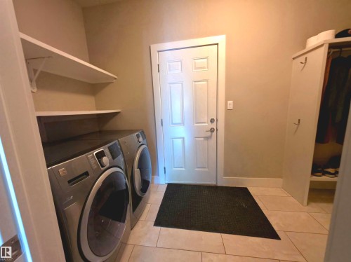Utility room featuring tile flooring, built-in shelving, a paneled door, and a built-in storage cabinet with hanging space - 1 Hemlock Close, Fort Saskatchewan, AB 