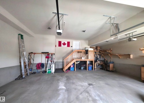 Spacious garage with overhead door mechanisms, concrete flooring, and built-in wooden shelving for storage - 1 Hemlock Close, Fort Saskatchewan, AB 