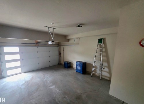 Spacious garage featuring a modern sectional garage door with frosted window panels, concrete flooring, and an overhead garage door opener system - 1 Hemlock Close, Fort Saskatchewan, AB 