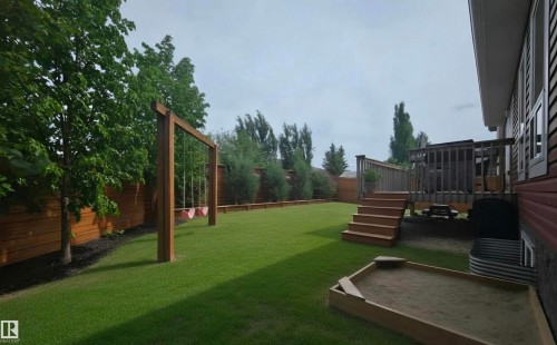 Expansive backyard featuring a manicured lawn, a wooden swing set, and a sandbox - 1 Hemlock Close, Fort Saskatchewan, AB 