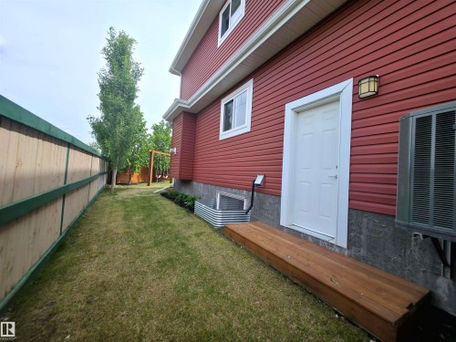 Red siding exterior with white trim, featuring a white entry door and exterior wall sconce - 1 Hemlock Close, Fort Saskatchewan, AB 