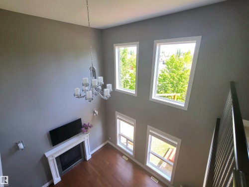Two-story living area featuring a fireplace with a white mantel, a polished chrome chandelier, and four windows providing natural light - 1 Hemlock Close, Fort Saskatchewan, AB 
