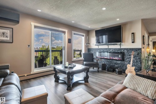 Living area featuring wood-finish flooring, recessed lighting, and a stone-accented wall with an electric fireplace - 305 5212 48 Avenue, Wetaskiwin, AB 