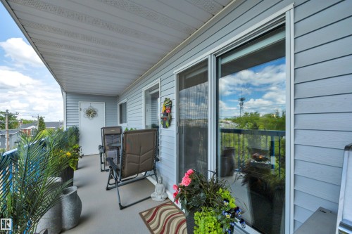 Covered outdoor balcony featuring light gray siding, white trim, a solid exterior door, and sliding glass patio doors - 305 5212 48 Avenue, Wetaskiwin, AB 