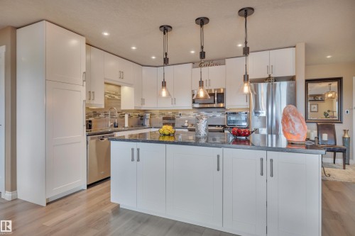 Modern kitchen featuring white cabinetry, dark countertops, stainless steel appliances, and wood-finish flooring - 305 5212 48 Avenue, Wetaskiwin, AB 