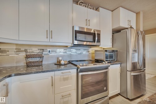 Kitchen featuring white shaker-style cabinetry, stainless steel appliances, a dark countertop, and a tiled backsplash - 305 5212 48 Avenue, Wetaskiwin, AB 