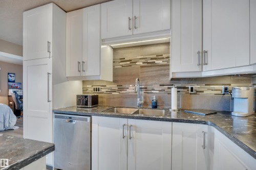 Modern kitchen featuring white cabinetry, stone-finish countertops, stainless steel dishwasher, and a mosaic tile backsplash - 305 5212 48 Avenue, Wetaskiwin, AB 