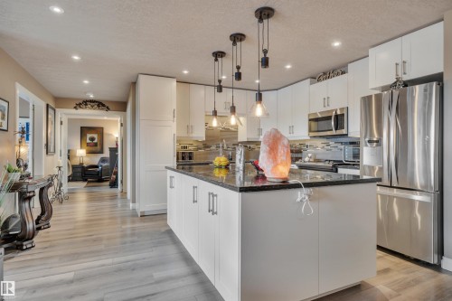 Kitchen featuring an island with a dark countertop, white cabinetry, stainless steel appliances, and pendant lighting - 305 5212 48 Avenue, Wetaskiwin, AB 