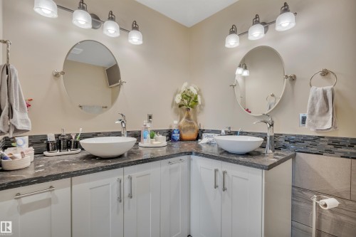 Bathroom featuring dual vessel sinks, white shaker-style cabinetry, and dark countertops with a mosaic tile backsplash - 305 5212 48 Avenue, Wetaskiwin, AB 