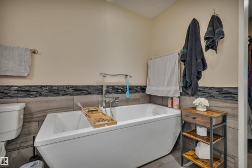 Freestanding soaking tub with chrome fixtures, complemented by a tiled surround featuring a mosaic accent band - 305 5212 48 Avenue, Wetaskiwin, AB 