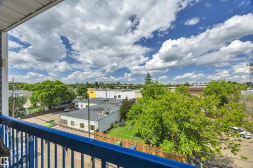 Balcony featuring a blue metal railing, offering overhead views of residential and commercial structures, green trees, and a clear sky with clouds - 305 5212 48 Avenue, Wetaskiwin, AB 