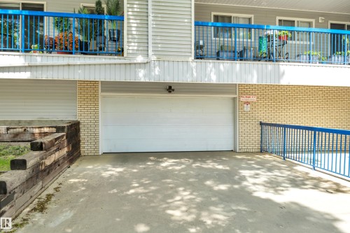 Underground garage entrance with a white sectional door, framed by light-colored brick siding - 305 5212 48 Avenue, Wetaskiwin, AB 