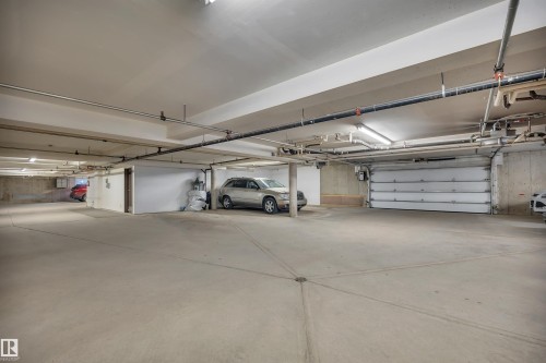 Underground parking garage featuring concrete flooring, exposed ceiling utilities, fluorescent lighting fixtures, and an automatic sectional garage door - 305 5212 48 Avenue, Wetaskiwin, AB 