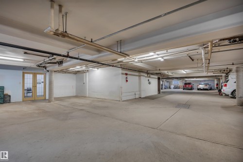 Subterranean parking garage with concrete flooring, exposed ceiling pipes, and fluorescent lighting - 305 5212 48 Avenue, Wetaskiwin, AB 