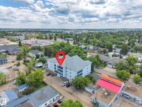 Four-story multi-unit building featuring a light-colored exterior and multiple balconies, surrounded by mature trees - 305 5212 48 Avenue, Wetaskiwin, AB 