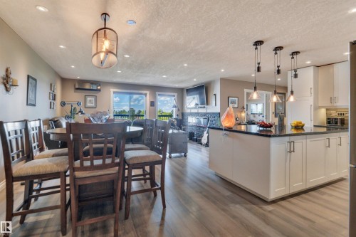Open-concept living space featuring wood-finish flooring, recessed lighting, and a contemporary kitchen with white shaker cabinetry, dark countertops, and pendant lighting - 305 5212 48 Avenue, Wetaskiwin, AB 