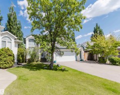 Light-colored siding exterior featuring a prominent arched window, an attached two-car garage, and mature landscaping - 