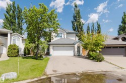 White exterior with an attached garage, paved driveway, and a front yard featuring a mature tree and green lawn - 