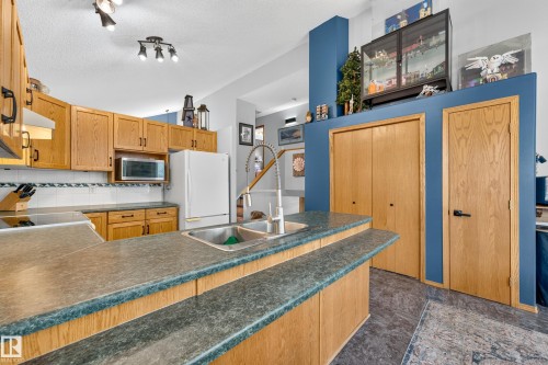 Kitchen featuring light wood cabinetry with dark hardware, a dual basin stainless steel sink with a high-arch faucet, and a two-tiered breakfast bar - 1 Primrose Boulevard, Sherwood Park, AB 