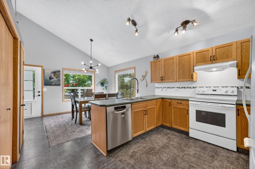 Open-concept kitchen and dining area featuring vaulted ceilings, wood-finish cabinetry, white tile backsplash, and dark tile flooring - 1 Primrose Boulevard, Sherwood Park, AB 