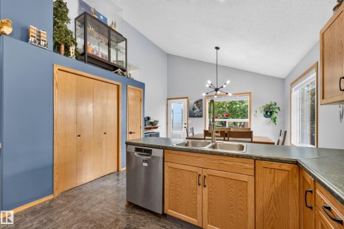 Kitchen area featuring warm wood cabinetry with dark hardware, a stainless steel dishwasher, and a double basin sink with a gooseneck faucet - 1 Primrose Boulevard, Sherwood Park, AB 