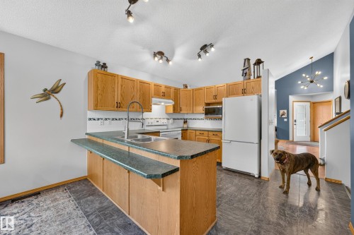 Kitchen featuring wood-finish cabinetry, dark countertops, and a white tile backsplash - 1 Primrose Boulevard, Sherwood Park, AB 