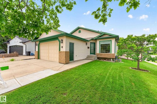 Exterior featuring beige siding with green trim accents, an attached two-car garage, a covered front entry, bay window, and a manicured front lawn - 1 Primrose Boulevard, Sherwood Park, AB 