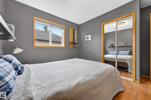 Bedroom featuring wood-finish flooring, a window with wood trim, and a mirrored sliding closet door - 1 Primrose Boulevard, Sherwood Park, AB 
