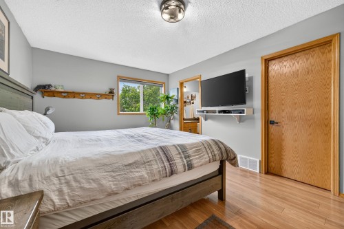Bedroom featuring light wood-finish flooring, a wood-trimmed window, a flush-mount ceiling light fixture, and a wall-mounted entertainment shelf - 1 Primrose Boulevard, Sherwood Park, AB 