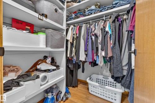 Walk-in closet featuring built-in shelving, hanging rods, light-toned walls, and wood-finish flooring - 1 Primrose Boulevard, Sherwood Park, AB 