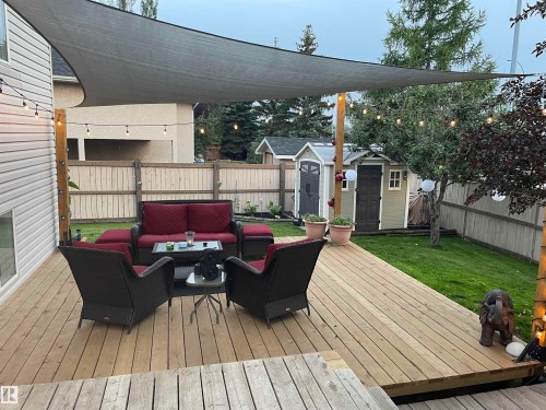 Expansive wood deck with a partial shade sail, string lighting, and direct access to a manicured lawn - 1 Primrose Boulevard, Sherwood Park, AB 