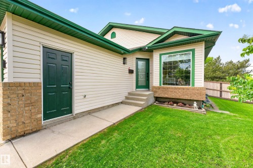 Exterior featuring cream-colored siding, contrasting green trim, and a prominent front bay window with brick accents - 1 Primrose Boulevard, Sherwood Park, AB 