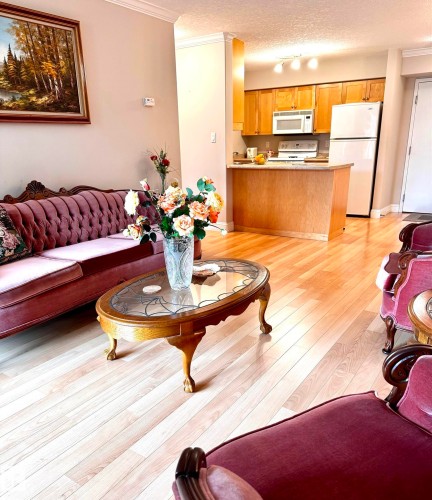 Open-concept living space featuring wood-finish flooring, crown molding, and a kitchen with light wood cabinetry - 330 13111 140 Avenue, Edmonton, AB 