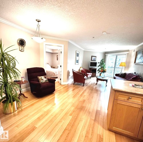 Open-concept living space with light wood-finish flooring, crown molding, a sliding glass door, and a built-in kitchen island with a light-toned countertop - 330 13111 140 Avenue, Edmonton, AB 