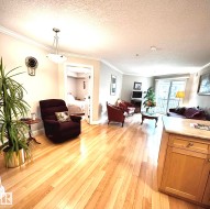 Open-concept living space with light wood-finish flooring, crown molding, a sliding glass door, and a built-in kitchen island with a light-toned countertop - 
