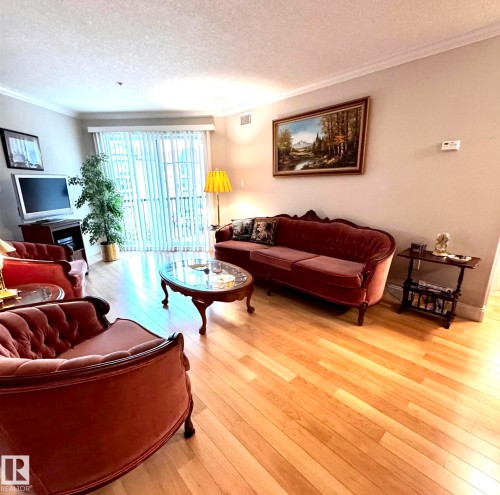 Living room featuring light wood-finish flooring, white crown molding, and vertical blinds on the patio door - 330 13111 140 Avenue, Edmonton, AB 