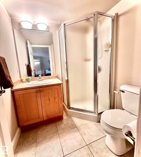 Bathroom featuring a corner shower enclosure with frosted glass, a light wood-finish vanity with an integrated sink, and an overhead lighting fixture - 330 13111 140 Avenue, Edmonton, AB 