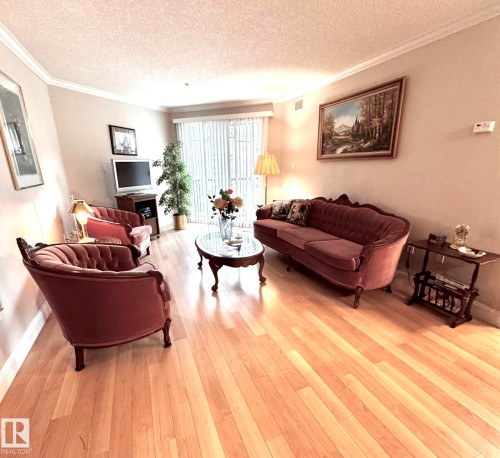 Living area featuring light wood-finish flooring, crown molding, and a sliding glass door with vertical blinds - 330 13111 140 Avenue, Edmonton, AB 