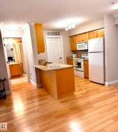 Kitchen area featuring a light wood-finish island with a light-toned countertop, ample natural wood cabinetry, and a suite of white appliances - 