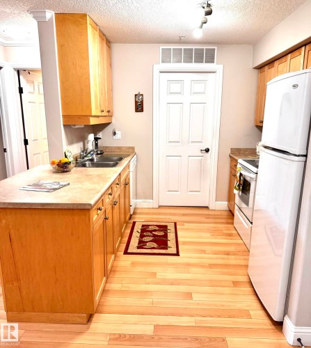 Kitchen featuring light wood-finish flooring, light wood cabinetry, white appliances, and a double basin sink - 330 13111 140 Avenue, Edmonton, AB 