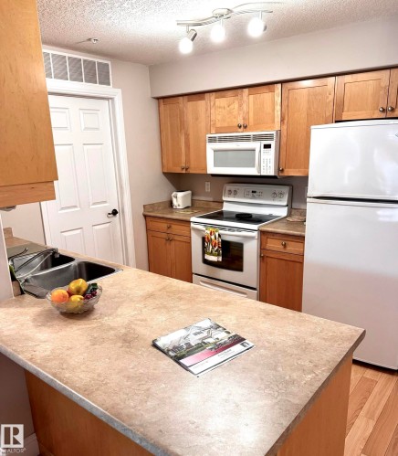 Kitchen featuring light wood-finish cabinetry, a double basin stainless steel sink, track lighting, light-colored countertops, and wood-finish flooring - 330 13111 140 Avenue, Edmonton, AB 
