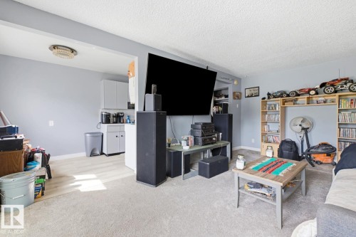Carpeted main living area featuring a built-in entertainment center and shelving, light gray wall paint, and a textured ceiling - 15 10164 150 Street, Edmonton, AB 