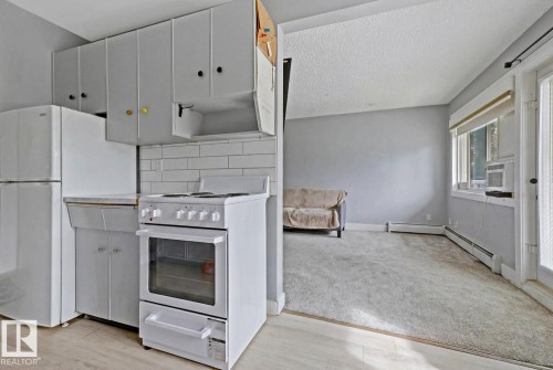Compact kitchen featuring white appliances, subway tile backsplash, light grey cabinetry, and wood-finish flooring - 15 10164 150 Street, Edmonton, AB 