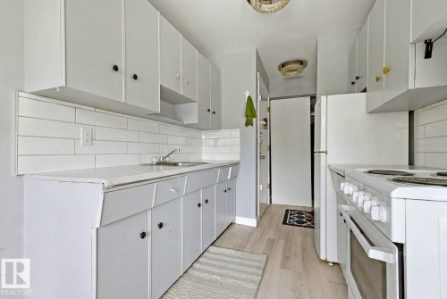 Bright kitchen featuring white cabinetry, a white subway tile backsplash, light wood-finish flooring, and a white freestanding range - 15 10164 150 Street, Edmonton, AB 